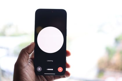 Mão segurando um smartphone com uma interface de assistente de voz exibida na tela.