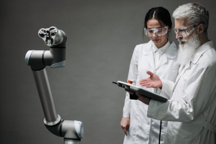 Pesquisadores usando jalecos e óculos de proteção analisam um braço robótico em um laboratório.