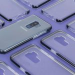 Close-up de um smartphone Samsung cercado por capas transparentes sobre uma superfície roxa.