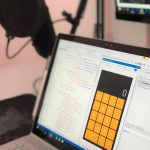 Laptop exibindo código e uma aplicação de calculadora em uma estação de trabalho moderna.
