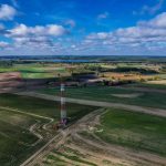 Torre de rádio isolada em meio a uma área rural sob céu azul