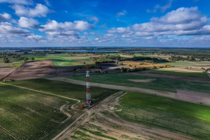Torre de rádio isolada em meio a uma área rural sob céu azul