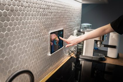 Painel touchscreen de controle de uma casa inteligente integrado à parede de uma cozinha moderna.