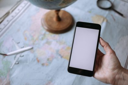 Mão segurando um smartphone sobre um mapa-múndi, ao lado de um globo e de um avião de brinquedo, simbolizando o planejamento de viagens.