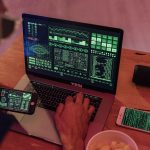 Homem trabalha com softwares de cibersegurança em um laptop e um smartphone.