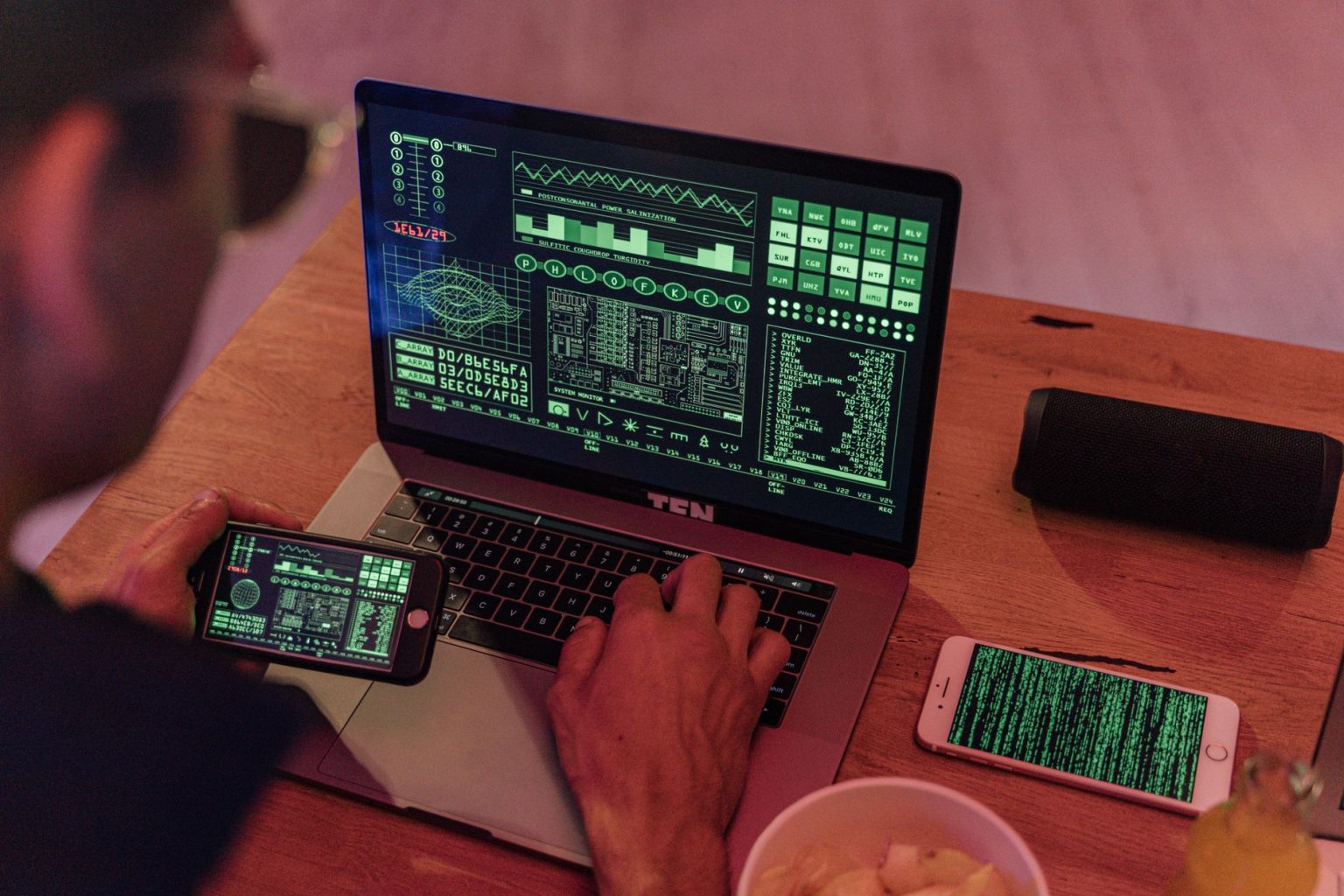 Homem trabalha com softwares de cibersegurança em um laptop e um smartphone.