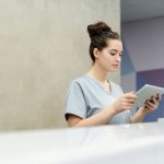 Profissional da recepção usa um tablet no balcão de uma clínica moderna.