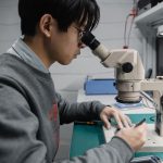 Técnico observa uma placa eletrônica ao microscópio em um laboratório de pesquisa.