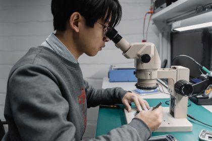 Técnico observa uma placa eletrônica ao microscópio em um laboratório de pesquisa.