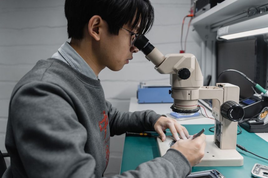Técnico observa uma placa eletrônica ao microscópio em um laboratório de pesquisa.