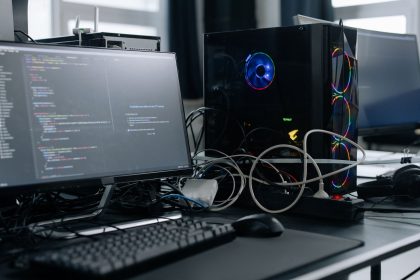 Estação de trabalho com monitor exibindo código, torre de computador e periféricos sobre uma mesa.